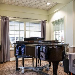 A grand piano in a well-lit music room with large windows and elegant curtains.
