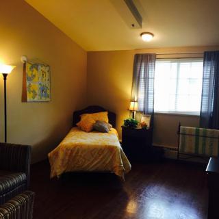 A cozy bedroom with a single bed, lamp, and window with curtains.