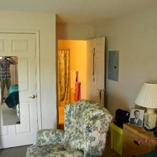 A cozy bedroom featuring a patterned chair, lamp, mirror, and an open door leading to another area.