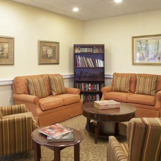 A cozy living room with comfortable sofas and chairs, a coffee table with magazines, and a bookshelf.