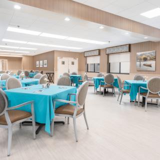 A spacious dining area with tables covered in blue tablecloths and neatly arranged chairs.