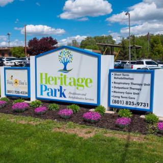 A sign for Heritage Park surrounded by colorful flowers on a sunny day.