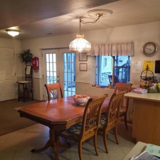 A cozy dining area with a wooden table and chairs, adjacent to a kitchen space, and well-lit by overhead lighting.