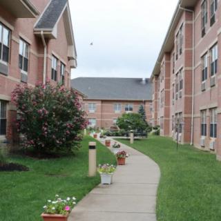 A well-maintained apartment complex with brick buildings, a landscaped sidewalk, and potted plants.