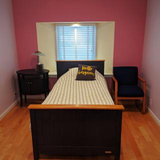 A simple bedroom setup with a single bed, nightstand, chair, and window.