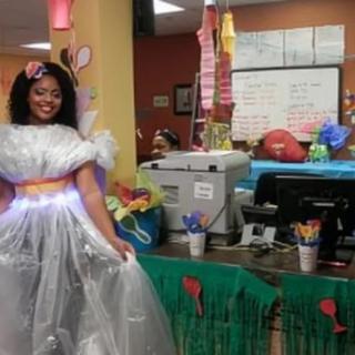 A person dressed in a creative costume stands in a festively decorated office setting.