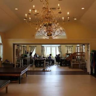 A spacious interior featuring a grand chandelier and mirrored walls, possibly a dance studio.