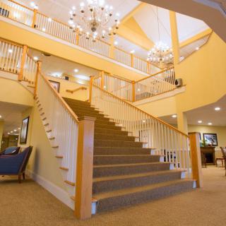 A spacious lobby featuring a grand staircase with wooden railings and a large chandelier.