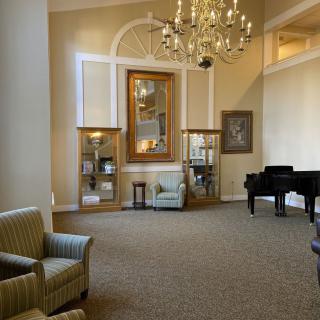 A spacious and elegantly decorated lounge area featuring a grand piano and chandelier.