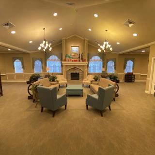 A spacious and elegantly decorated living room with chandeliers, a central fireplace, and comfortable seating arrangement.