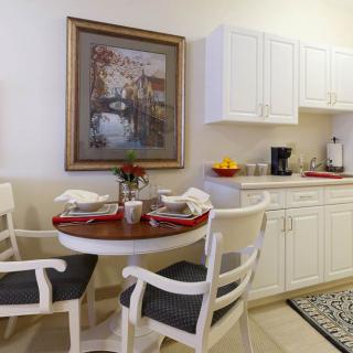 A small, modern kitchen area featuring a round table set for dining, with white cabinets and stylish artwork on the wall.
