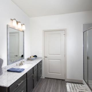 A modern bathroom featuring a large mirror, dual sinks, and a glass shower.