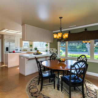 A cozy dining area adjacent to a modern kitchen, featuring a wooden table with chairs, large windows, and a stylish chandelier.