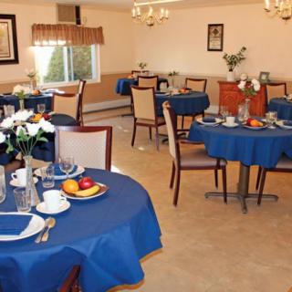A cozy dining room with elegantly set tables covered in blue tablecloths, adorned with flowers and dinnerware.