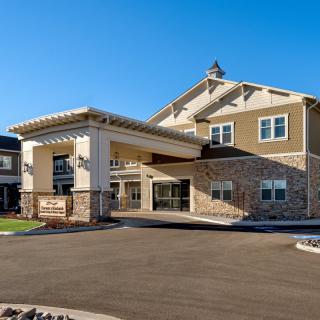 A modern building with a covered entrance, featuring a mix of stone and siding exterior under a clear blue sky.