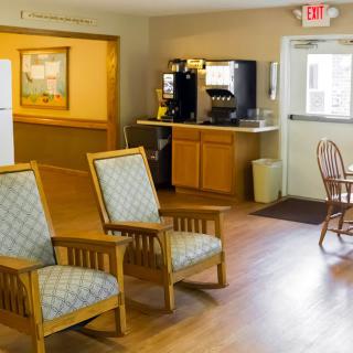 A cozy indoor waiting area with wooden chairs, a coffee machine, and wooden flooring.