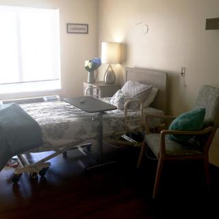 A hospital room with a bed, chair, and lamp near a window.