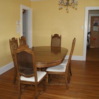 A dining room with a wooden table and four chairs, featuring a chandelier and hardwood flooring.