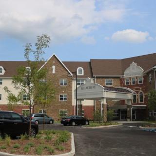 A residential building with a parking lot and landscaped surroundings on a cloudy day.