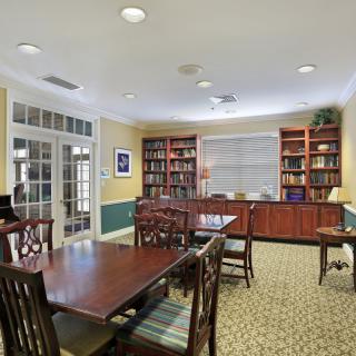 A cozy library room with wooden tables, chairs, and bookshelves filled with books.