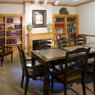 A cozy library room with bookshelves, a fireplace, and a large table surrounded by chairs.