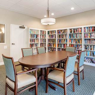 A cozy library meeting room with bookshelves lining the walls and a central table surrounded by chairs.