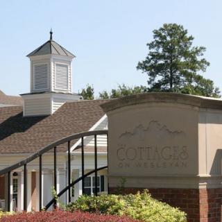 A building with a cupola in front of a sign, surrounded by trees and landscaping.