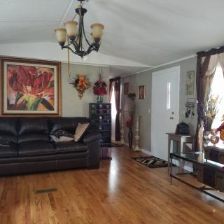 A cozy living room with a black leather couch, wooden floors, and decorative artwork on the walls.