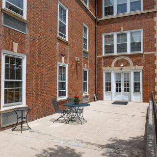 A sunny patio area with tables and chairs outside a brick building.