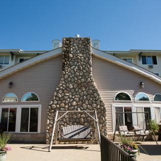 A house with a prominent stone chimney, featuring a swing and outdoor seating on the patio.