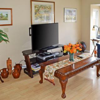A cozy living room featuring a television on a stand, a wooden coffee table adorned with flowers, and decorative vases and artwork.