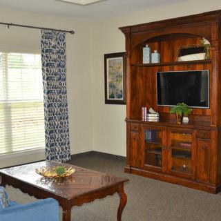 A cozy living room featuring a wooden entertainment center with a mounted TV, a coffee table, patterned curtains, and decor accents.