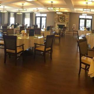A spacious and elegantly designed dining area with neatly arranged tables and chairs, illuminated by stylish chandeliers.