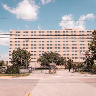 A tall apartment building with a gated entrance under a partly cloudy sky.