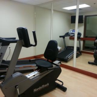A small gym with a treadmill and stationary bike in front of mirrored walls.