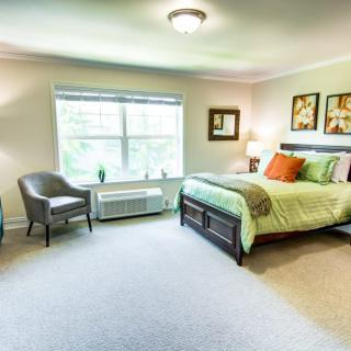 A well-lit bedroom featuring a comfortable bed, armchair, and decorative artwork.