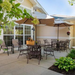 A cozy outdoor patio area with tables, chairs, and umbrellas in a garden setting.