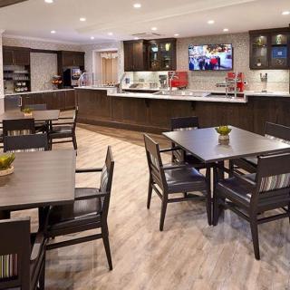 A modern dining area with tables and chairs, featuring a kitchenette and television.