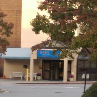The entrance to a hospital, surrounded by trees and a clear sky.