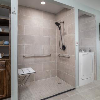 A modern, accessible walk-in shower with grab bars and a folding seat.