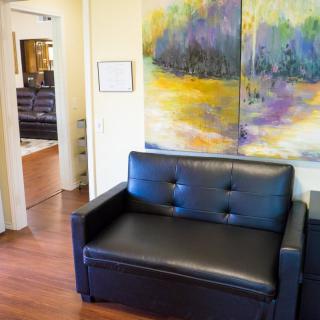A modern office waiting area featuring a black leather sofa and colorful abstract artwork on the wall.