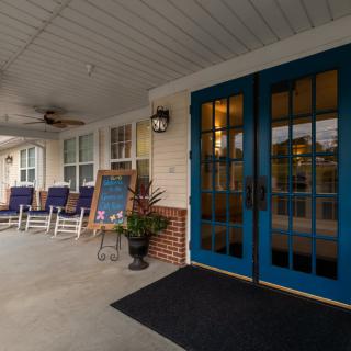 A cozy front porch with blue doors, rocking chairs, and a chalkboard sign.