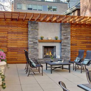 A cozy outdoor patio with a fireplace and comfortable seating under a wooden pergola in an urban setting.