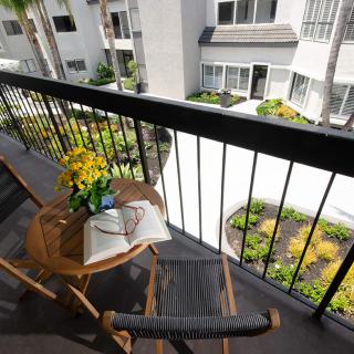 A cozy apartment balcony with a small table, a book, and flowers overlooking a residential courtyard.