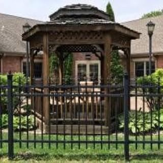 A wooden gazebo surrounded by a black metal fence in a garden setting.