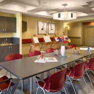 A modern conference room equipped with a large table, red chairs, and art easels in the background.