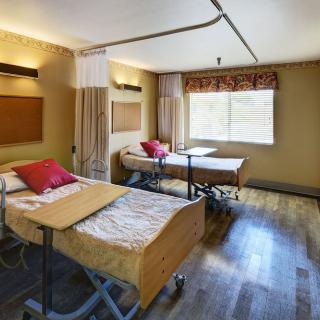 A modern hospital room with two medical beds, separated by privacy curtains and a window allowing natural light.