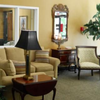 A cozy living room featuring a beige sofa, armchair, and a dark lamp on a wooden coffee table, with a decorative mirror on the wall.