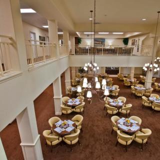 A spacious and elegant dining area with multiple tables set for service, featuring plush seating and decorative chandeliers.