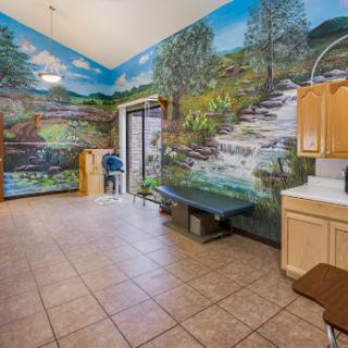 A spacious room featuring a vibrant nature mural, complete with a kitchenette and tiled flooring.